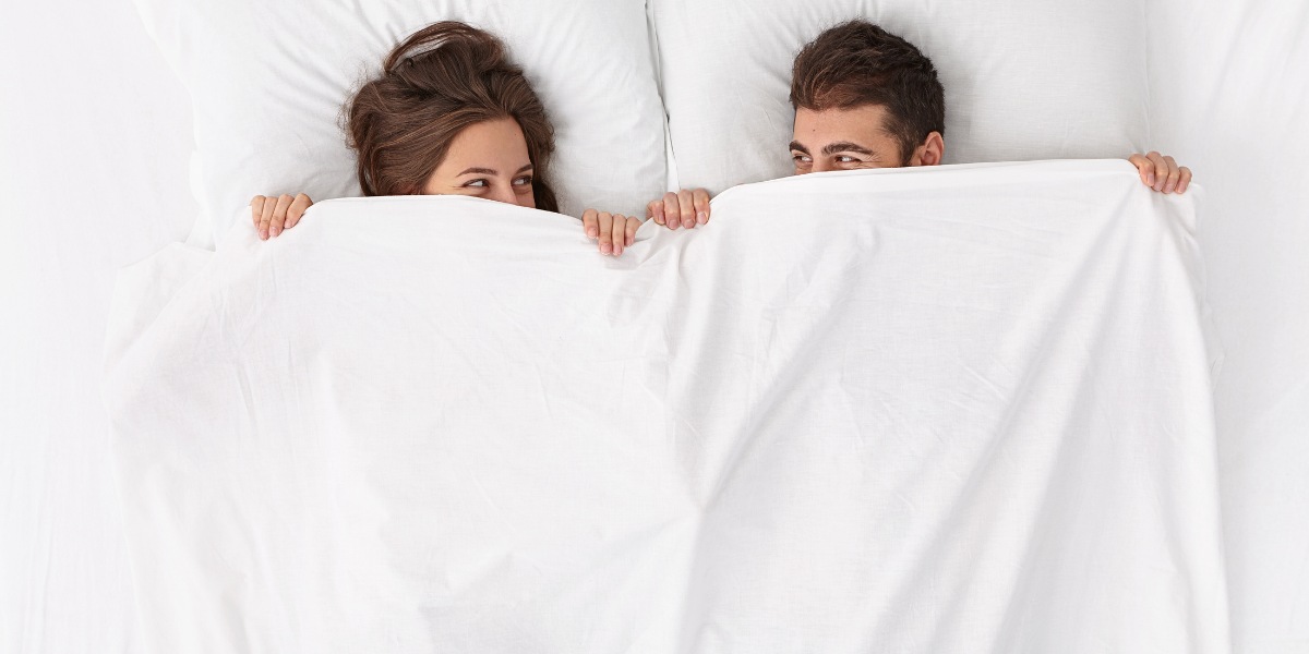 Couple lying in bed under a white blanket - Couple Transgression