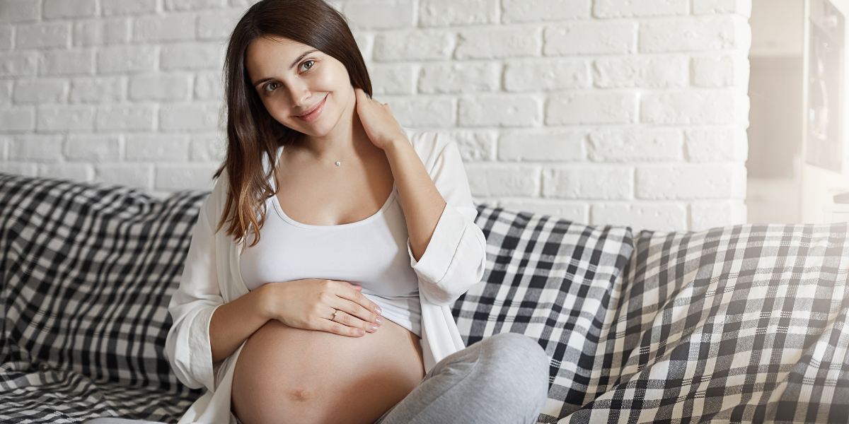 Young pregnant girl sitting on the sofa while looking at the camera