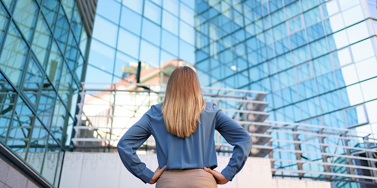 Rear view of a female manager observing a commercial building in broad daylight with her hands on her hips